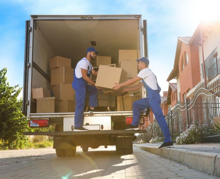 Two movers passing a box into the back of a removal truck on a sunny street