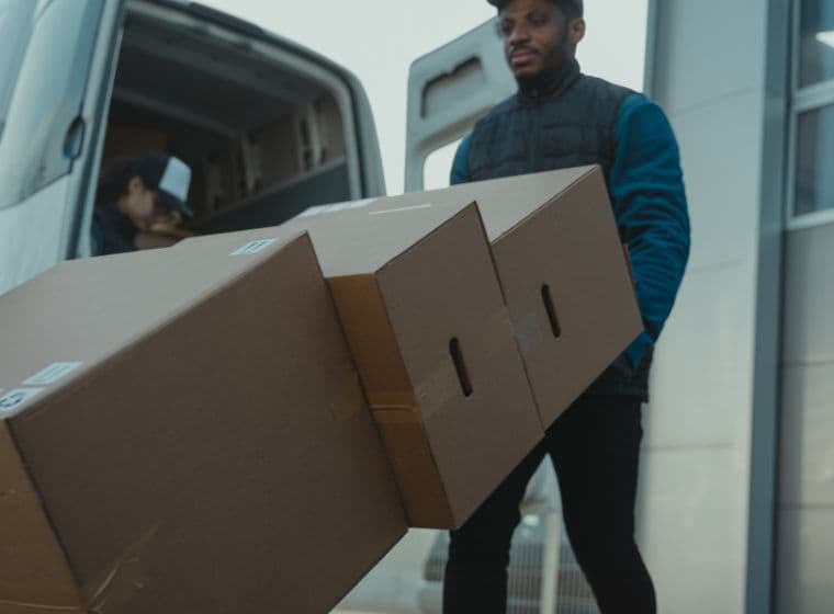 Two movers carrying long cardboard boxes from a van