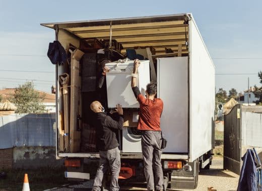 Two movers lifting a large appliance into the back of a removal truck